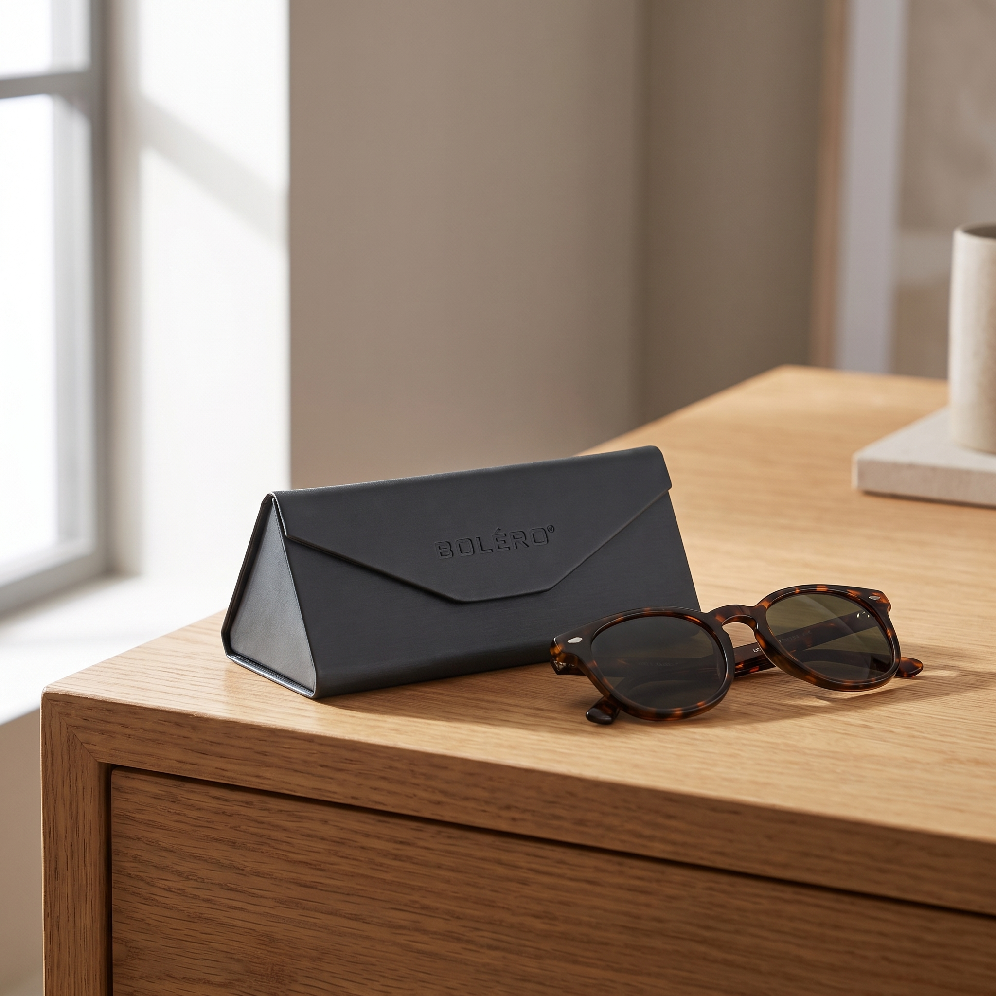 Bolero hard case on an oak desk beside a pair of tortoise sunglasses